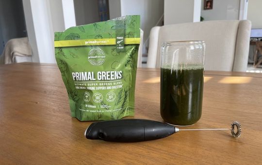 mixed glass of primal greens next to a bag of primal greens in powder form